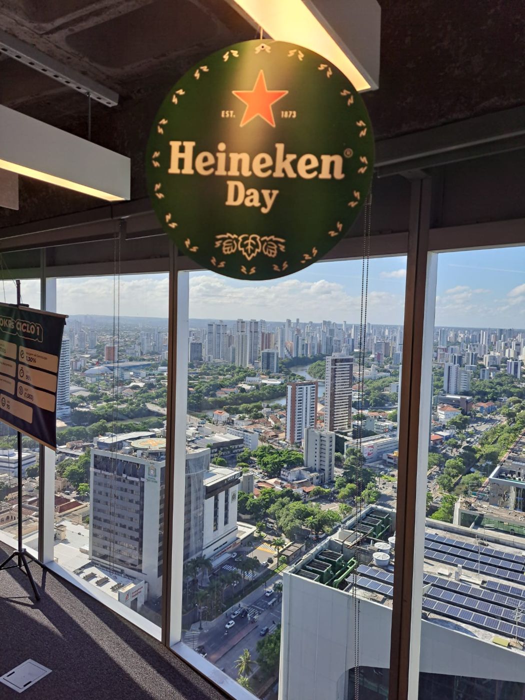 Placa do Heineken Day na janela, com Recife ao fundo